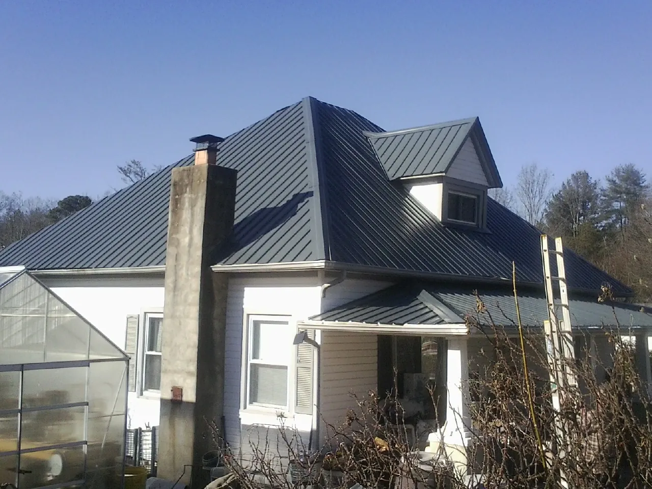 Dark blue standing seam metal roof on a white farmhouse with dormer — Slate & Tile Roof Repair by Roofing Brothers in East Flat Rock