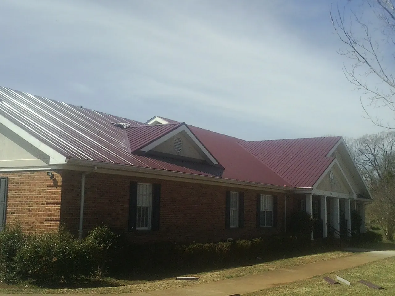 Red metal roof with gabled entries on a long brick building, from a Hail Damage Roof Repair job in East Flat Rock