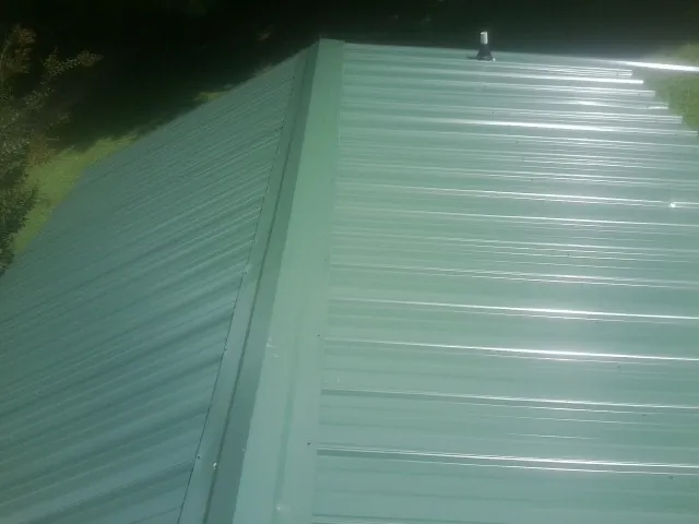 New green metal panels meeting at the ridge of a roof — Flat Roof Repair work by our crew in East Flat Rock