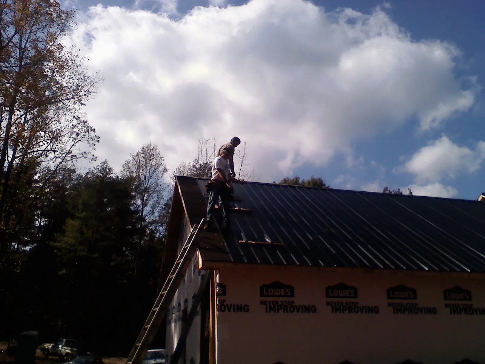 Roofer fastening dark metal panels high against a cloudy sky, from a Roof Inspection job in East Flat Rock