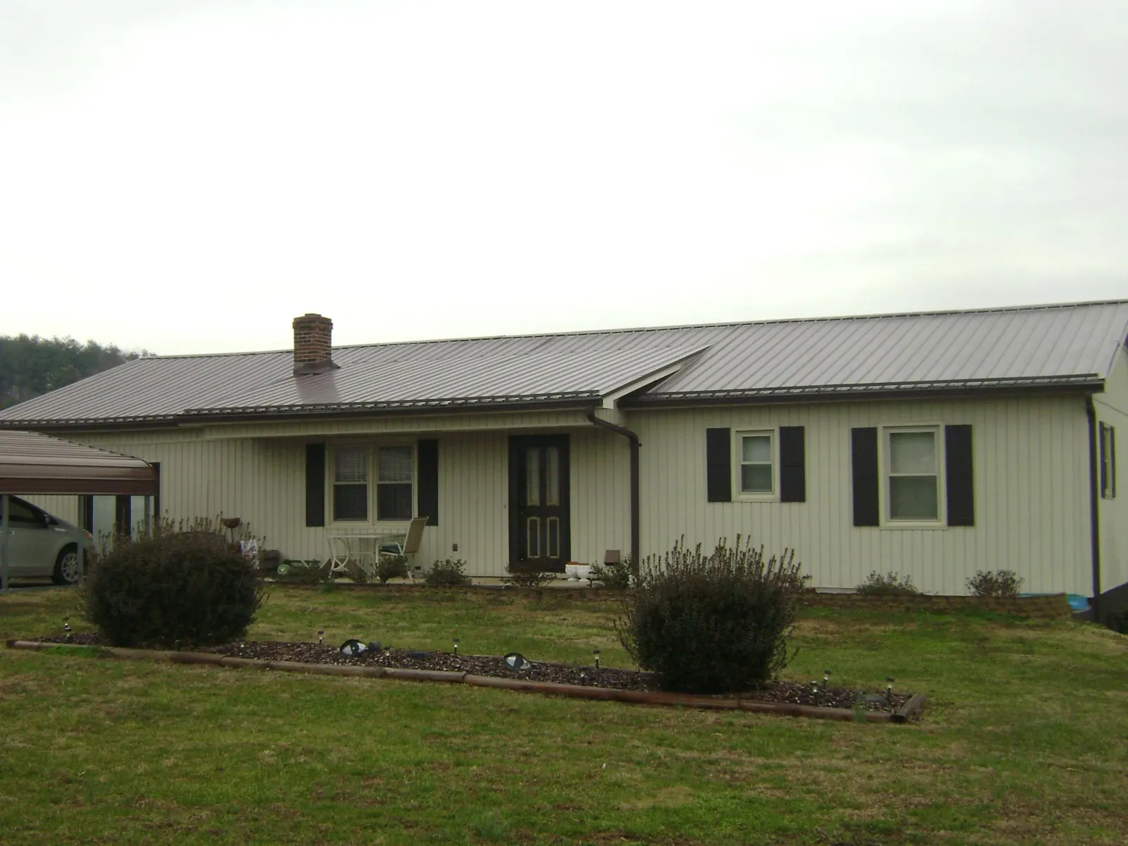 Brown metal roof on a cream sided ranch home with a brick chimney in East Flat Rock