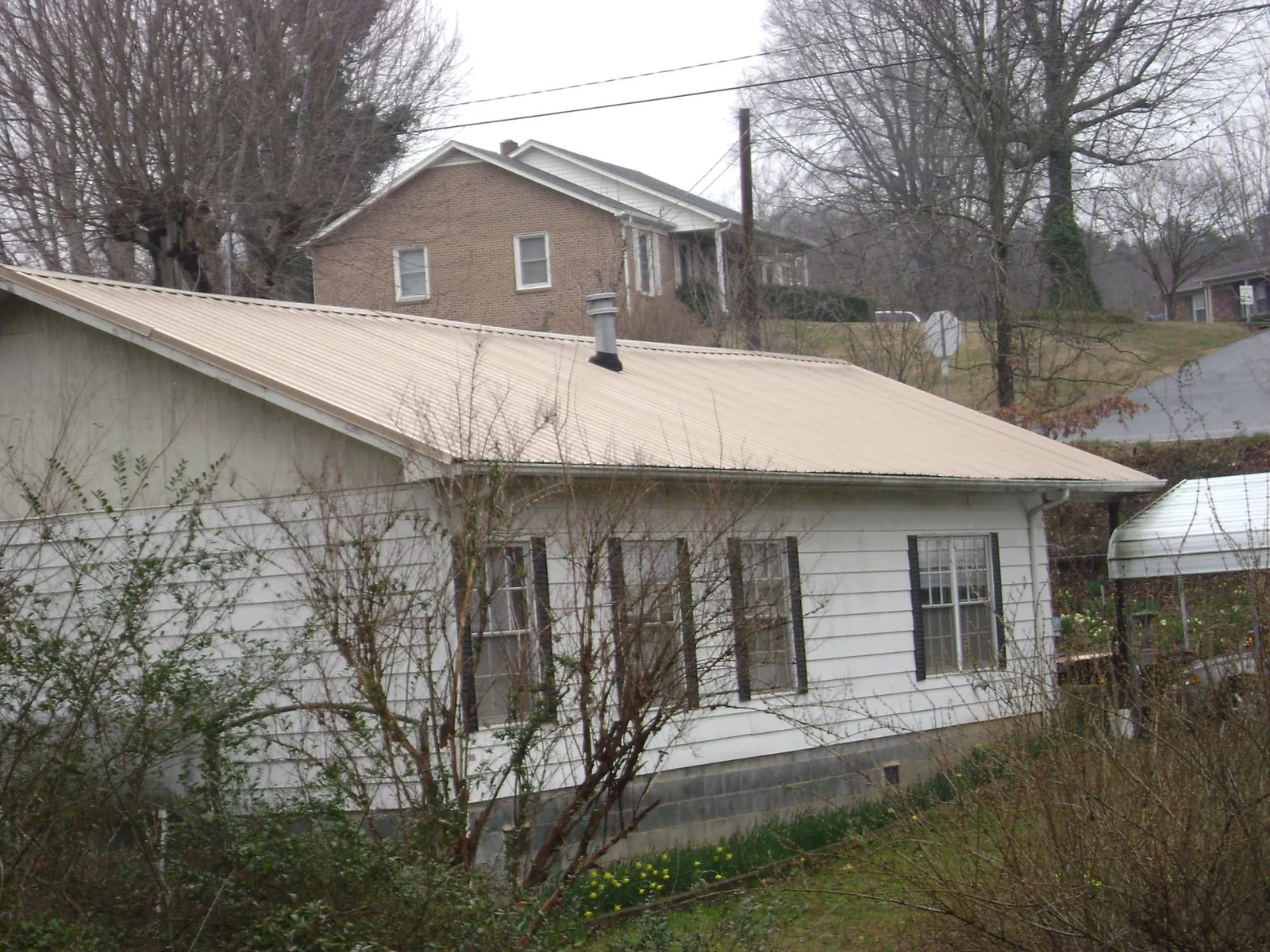 Tan metal roof on a white sided house set into a hillside — Commercial Roofing by Roofing Brothers in East Flat Rock