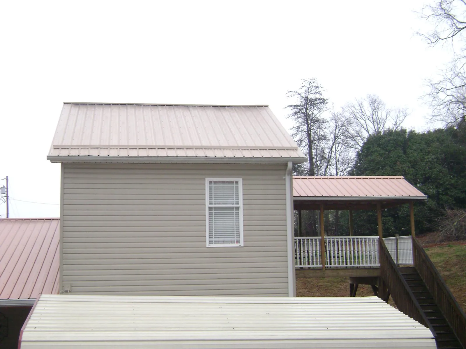 Tan metal roofs on a two story addition and attached porch, from a Roof Replacement job in East Flat Rock